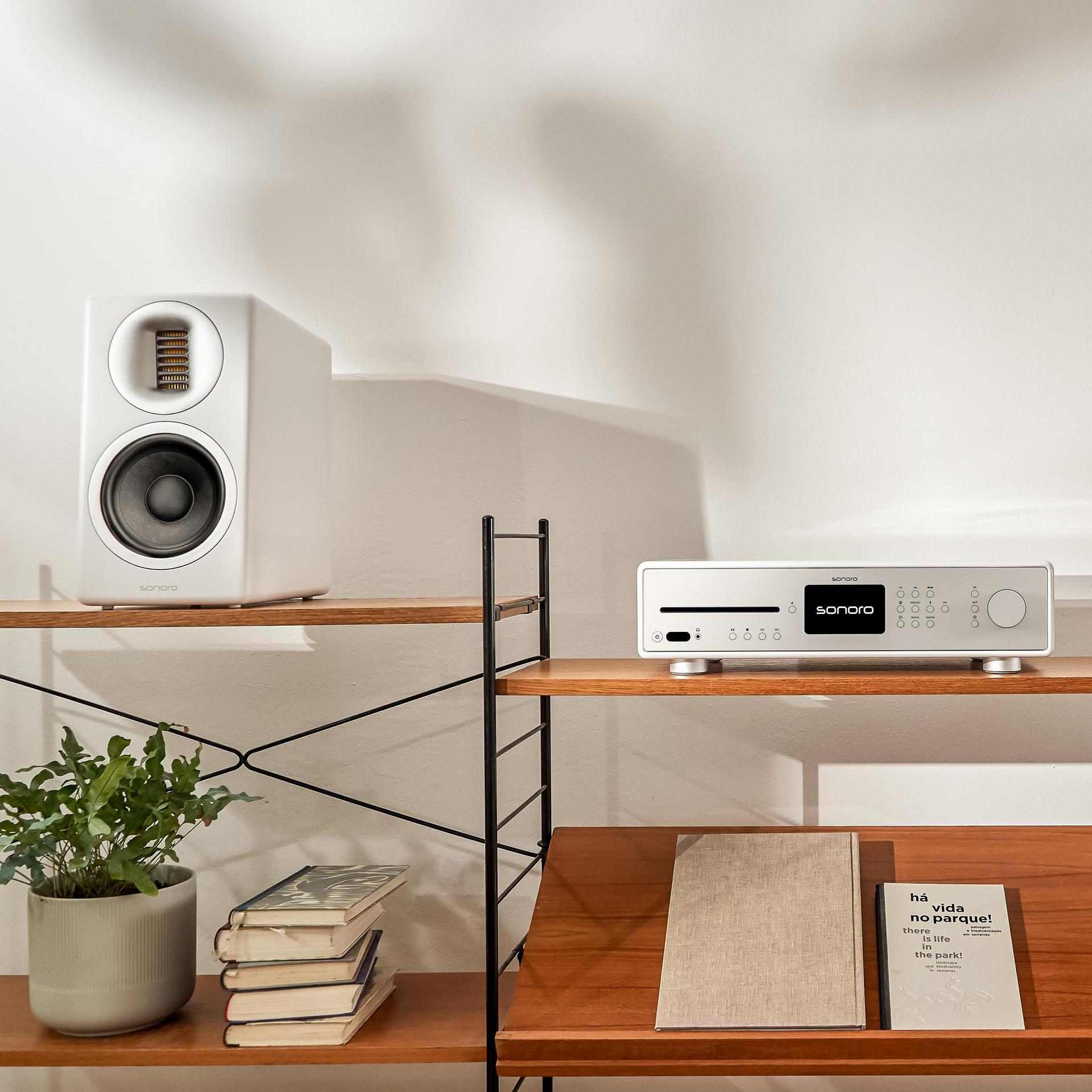Weißes sonoro Lautsprecherpaar mit HiFi-Gerät auf Regal – deutsche Ingenieurskunst in stilvoller Wohnumgebung.